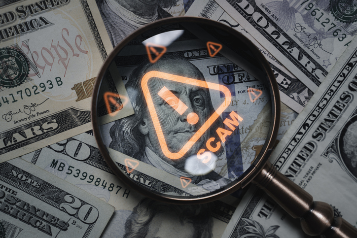 Magnifying glass focusing on scam warning symbol over dollar bills concept of financial fraud money laundering cybercrime and online scam alert for security awareness and finance protection